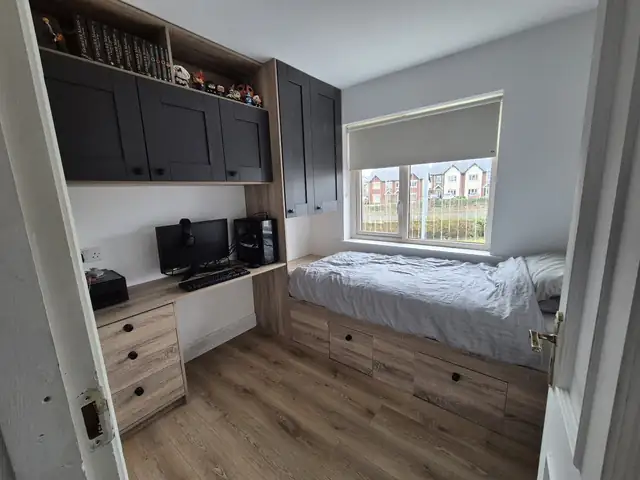 Box room with a built in desk, overhead cupboards and a bed with storage drawers